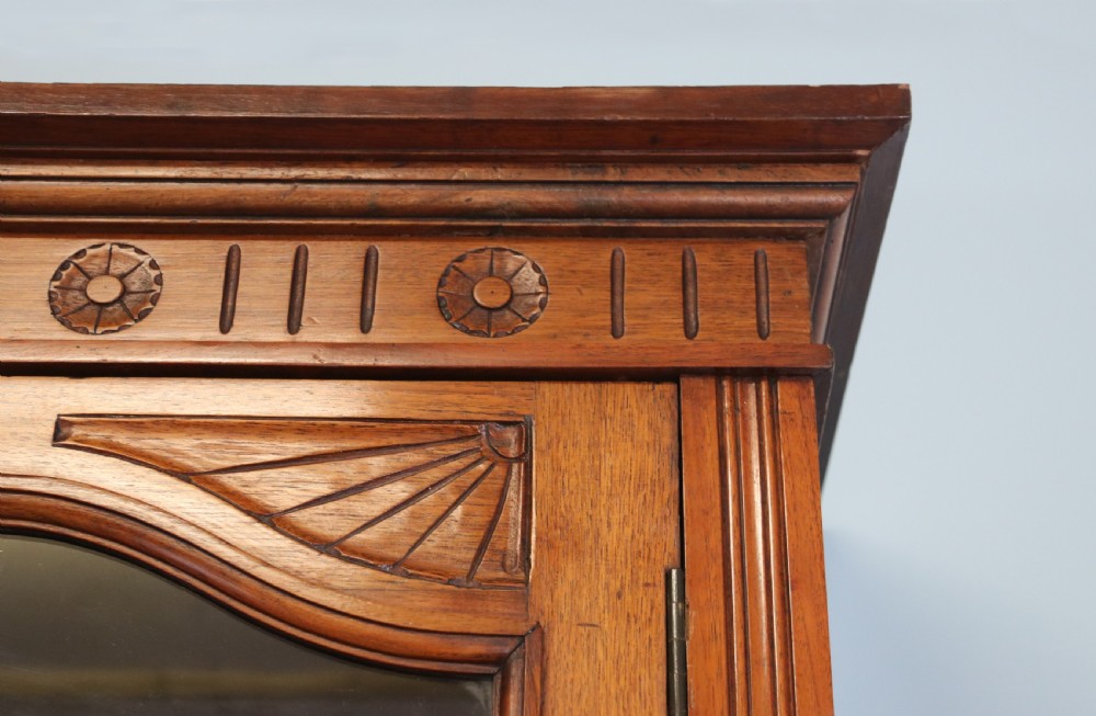 A two-tier dark walnut display cabinet featuring glazed upper doors decorated with vintage Cadburys advertising lettering above lower carved wooden cupboard doors. View X