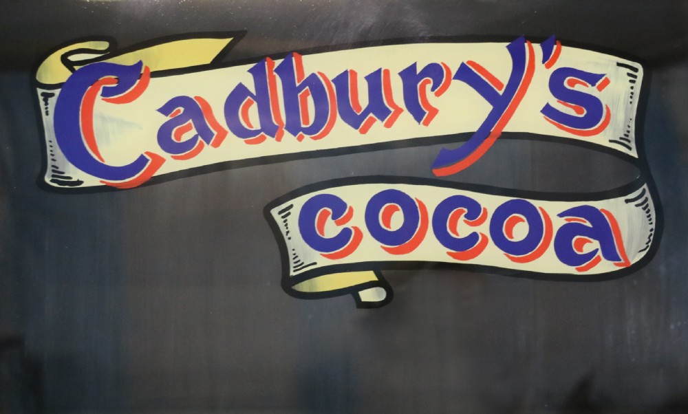 A two-tier dark walnut display cabinet featuring glazed upper doors decorated with vintage Cadburys advertising lettering above lower carved wooden cupboard doors. View XI