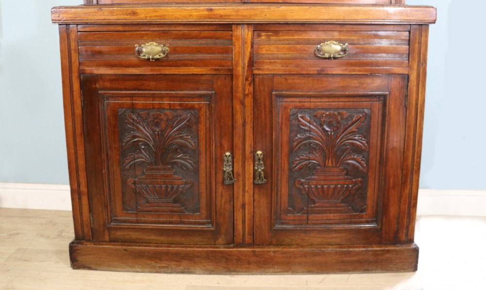 A two-tier dark walnut display cabinet featuring glazed upper doors decorated with vintage Cadburys advertising lettering above lower carved wooden cupboard doors. View XV