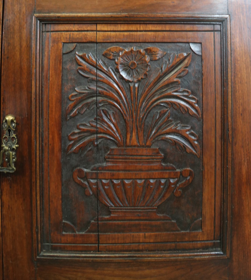 A two-tier dark walnut display cabinet featuring glazed upper doors decorated with vintage Cadburys advertising lettering above lower carved wooden cupboard doors. View XX