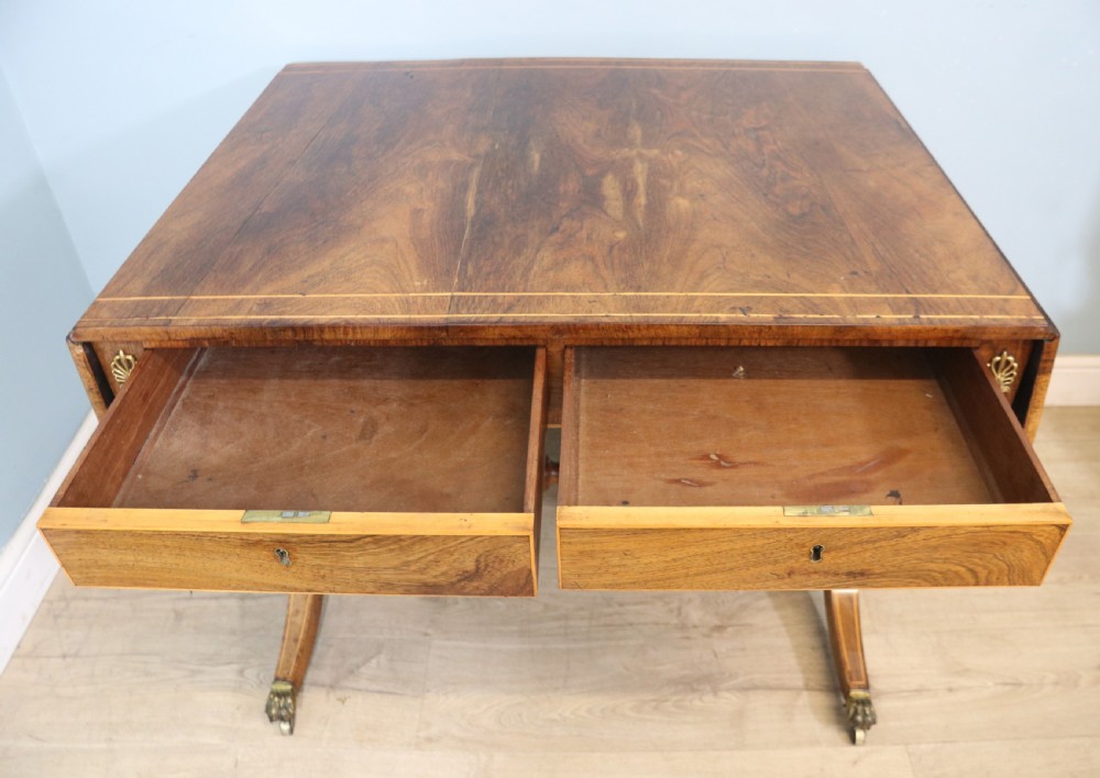An early 19th-century Regency drop-leaf sofa table made of polished dark wood with two drawers, brass mounts, turned stretcher, and splayed legs with brass paw castors. View VII