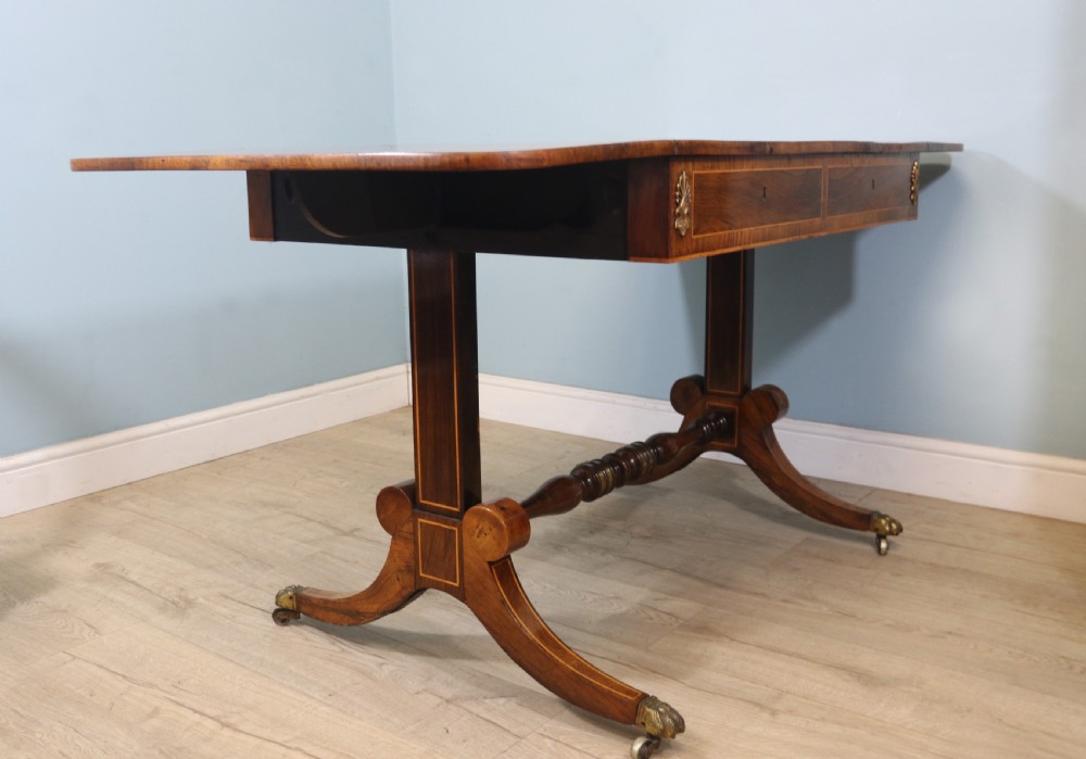 An early 19th-century Regency drop-leaf sofa table made of polished dark wood with two drawers, brass mounts, turned stretcher, and splayed legs with brass paw castors. View VIII