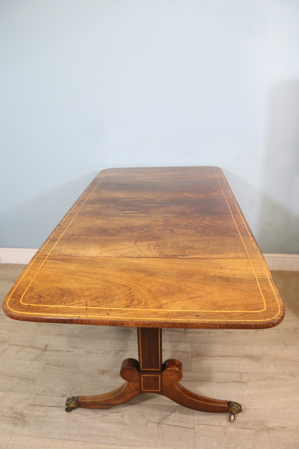 An early 19th-century Regency drop-leaf sofa table made of polished dark wood with two drawers, brass mounts, turned stretcher, and splayed legs with brass paw castors. View IX