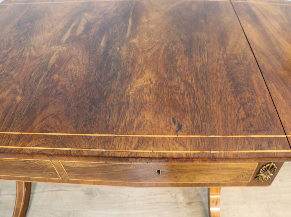 An early 19th-century Regency drop-leaf sofa table made of polished dark wood with two drawers, brass mounts, turned stretcher, and splayed legs with brass paw castors. View XII