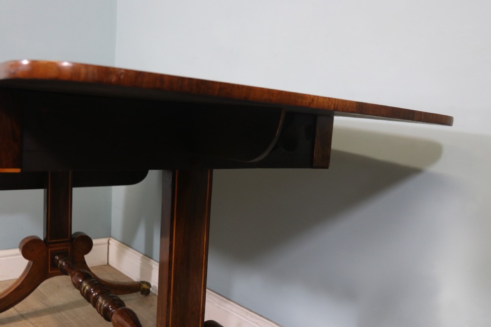 An early 19th-century Regency drop-leaf sofa table made of polished dark wood with two drawers, brass mounts, turned stretcher, and splayed legs with brass paw castors. View XVIII