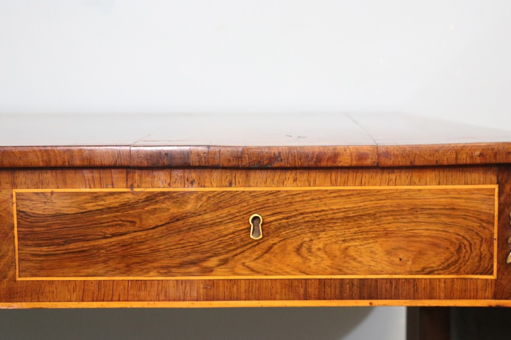 An early 19th-century Regency drop-leaf sofa table made of polished dark wood with two drawers, brass mounts, turned stretcher, and splayed legs with brass paw castors. View XX