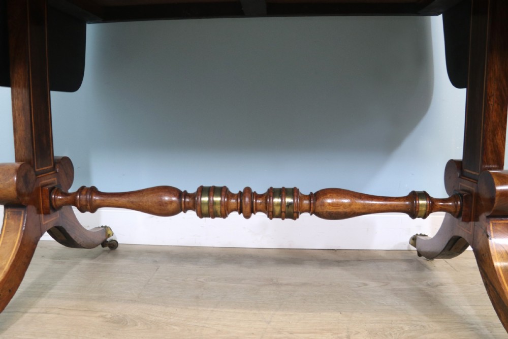 An early 19th-century Regency drop-leaf sofa table made of polished dark wood with two drawers, brass mounts, turned stretcher, and splayed legs with brass paw castors. View XXIV
