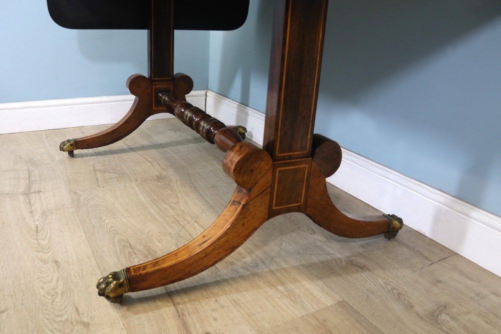 An early 19th-century Regency drop-leaf sofa table made of polished dark wood with two drawers, brass mounts, turned stretcher, and splayed legs with brass paw castors. View XXV
