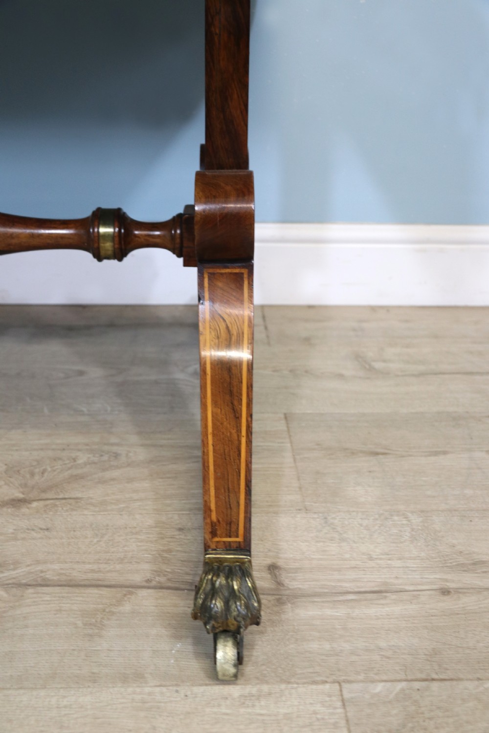 An early 19th-century Regency drop-leaf sofa table made of polished dark wood with two drawers, brass mounts, turned stretcher, and splayed legs with brass paw castors. View XXVI