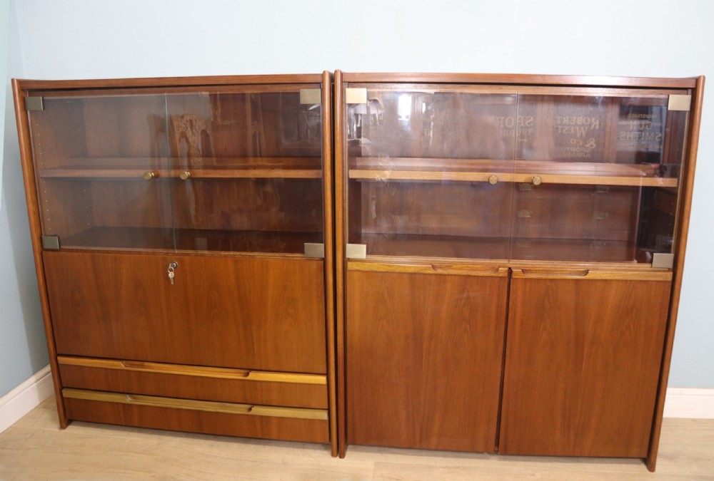 A pair of mid-century teak display cabinets featuring upper sliding glass doors, internal shelving, lower wooden cupboards, drawers, and brass fittings.