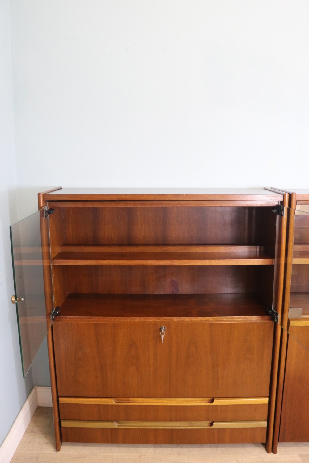 A pair of mid-century teak display cabinets featuring upper sliding glass doors, internal shelving, lower wooden cupboards, drawers, and brass fittings. View II