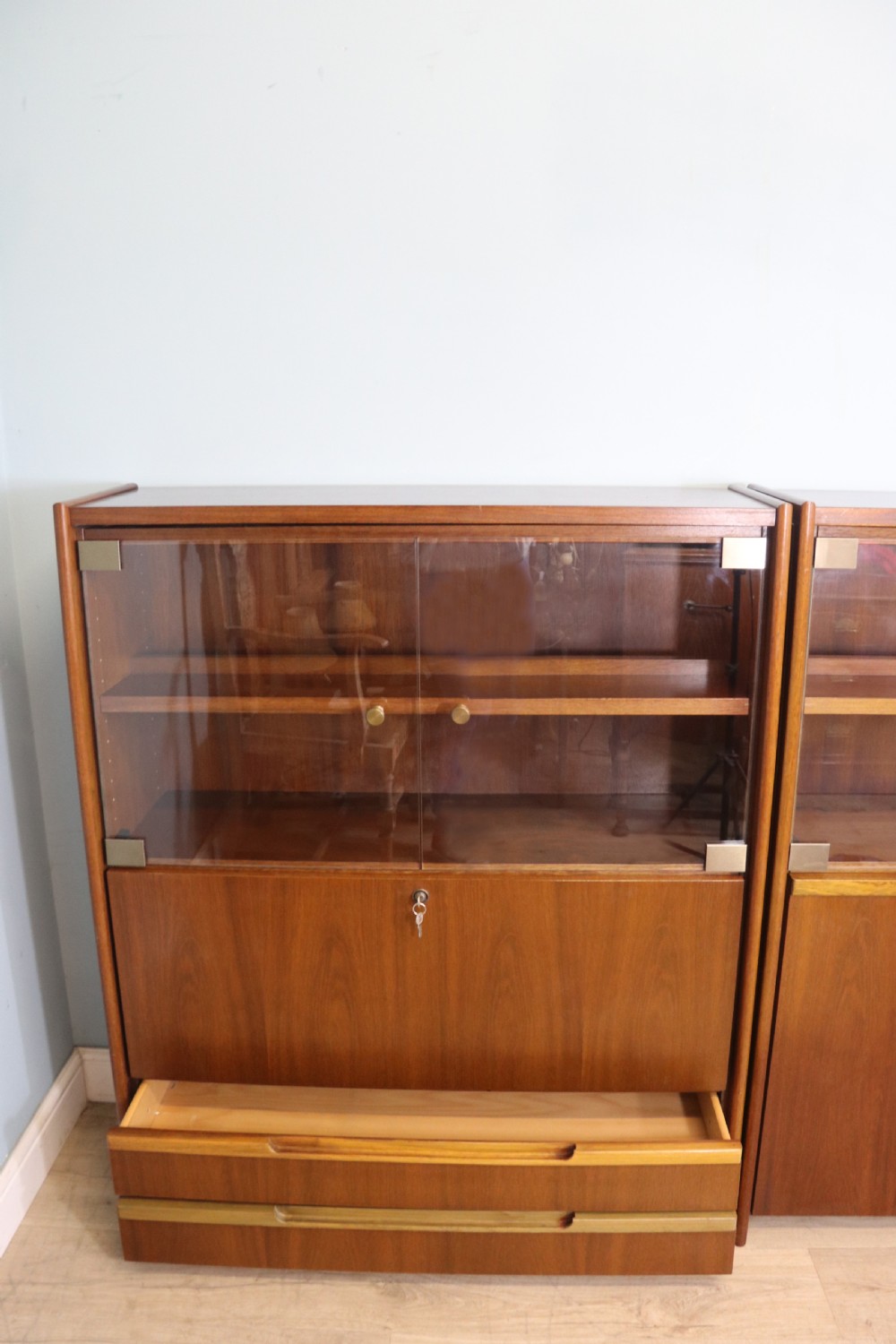 A pair of mid-century teak display cabinets featuring upper sliding glass doors, internal shelving, lower wooden cupboards, drawers, and brass fittings. View III