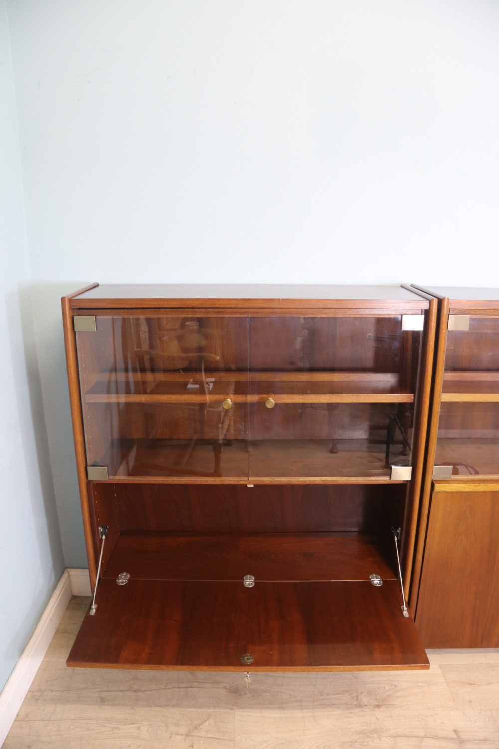 A pair of mid-century teak display cabinets featuring upper sliding glass doors, internal shelving, lower wooden cupboards, drawers, and brass fittings. View V