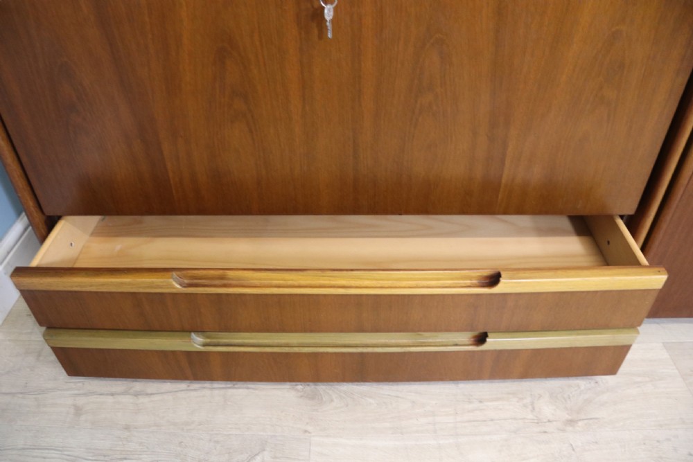 A pair of mid-century teak display cabinets featuring upper sliding glass doors, internal shelving, lower wooden cupboards, drawers, and brass fittings. View VII