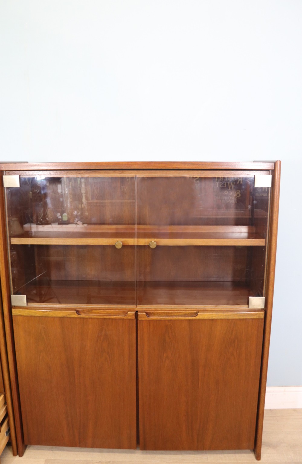 A pair of mid-century teak display cabinets featuring upper sliding glass doors, internal shelving, lower wooden cupboards, drawers, and brass fittings. View XI