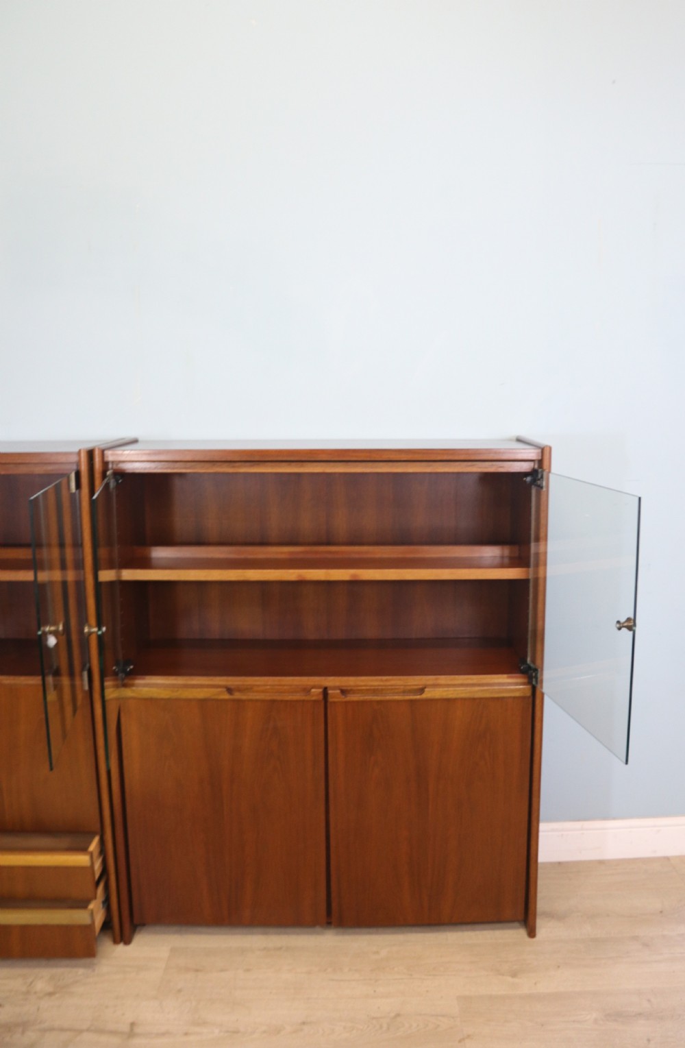 A pair of mid-century teak display cabinets featuring upper sliding glass doors, internal shelving, lower wooden cupboards, drawers, and brass fittings. View XII