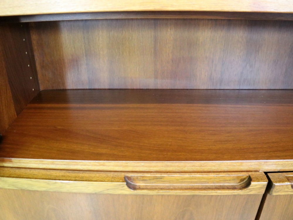 A pair of mid-century teak display cabinets featuring upper sliding glass doors, internal shelving, lower wooden cupboards, drawers, and brass fittings. View XV