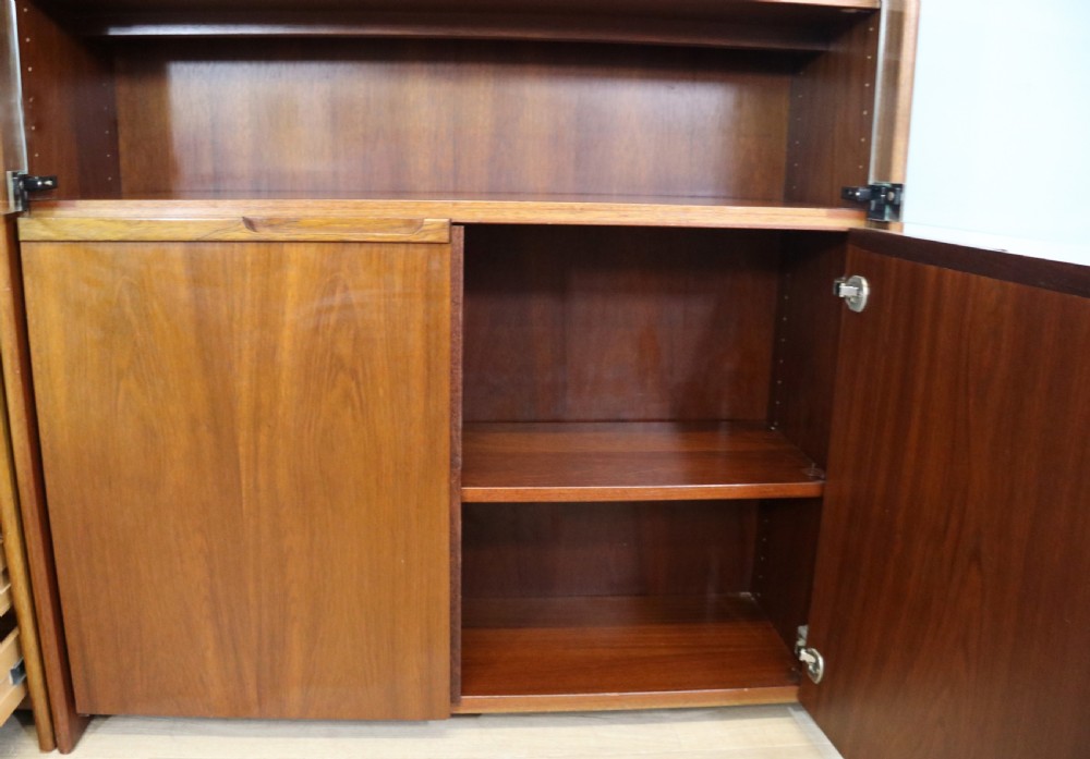 A pair of mid-century teak display cabinets featuring upper sliding glass doors, internal shelving, lower wooden cupboards, drawers, and brass fittings. View XVII