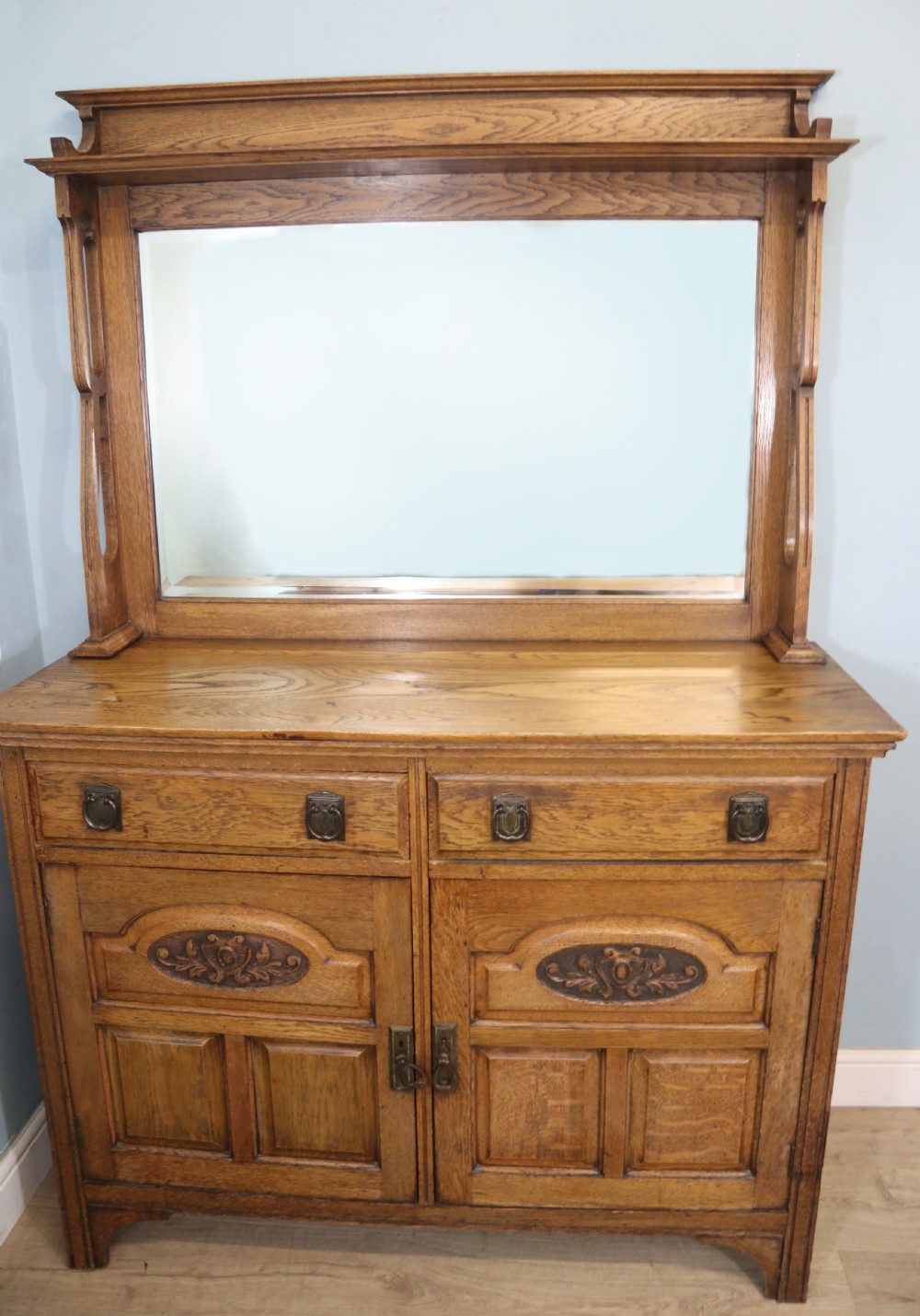 A late Victorian oak sideboard featuring a mirrored upper shelf, two drawers, and two carved panel cupboard doors.