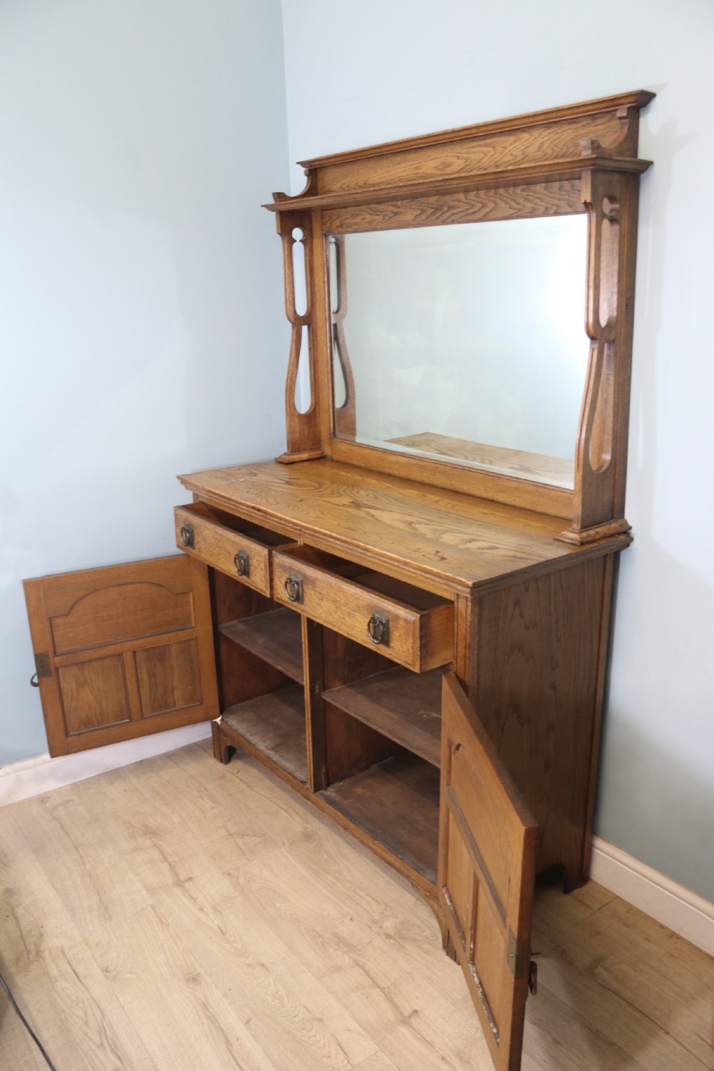 A late Victorian oak sideboard featuring a mirrored upper shelf, two drawers, and two carved panel cupboard doors. View III