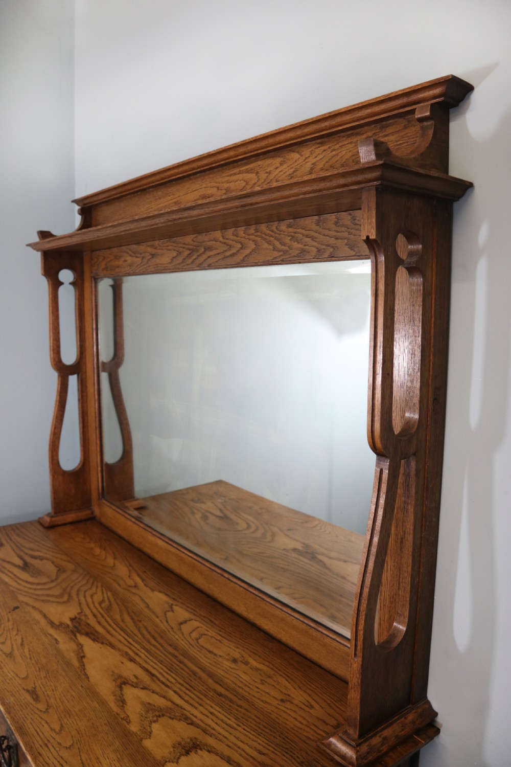 A late Victorian oak sideboard featuring a mirrored upper shelf, two drawers, and two carved panel cupboard doors. View IV