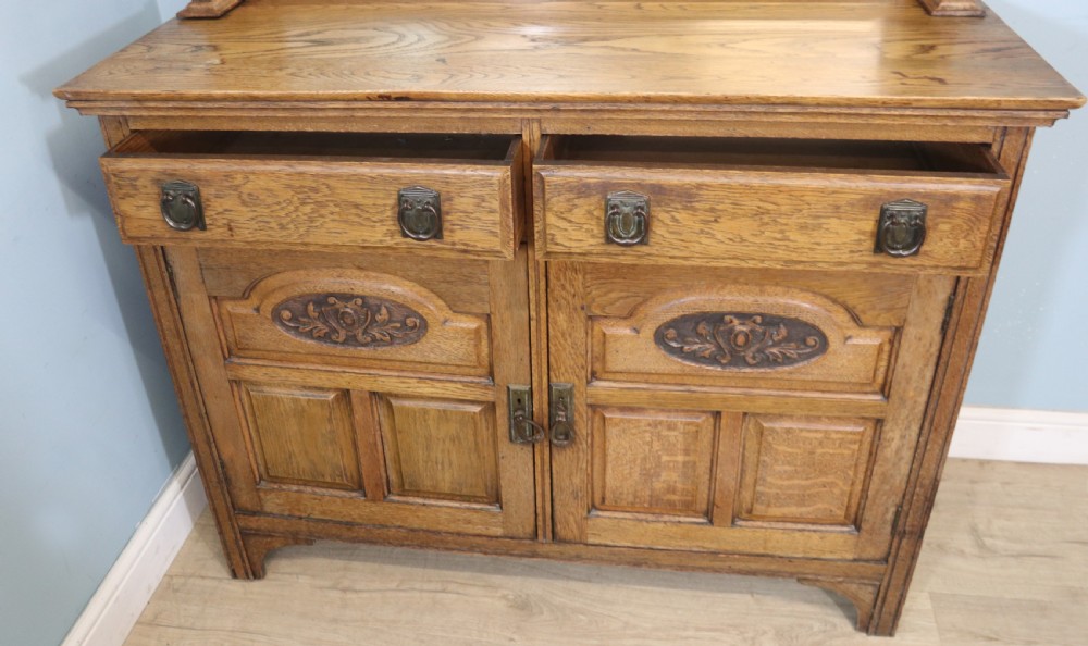 A late Victorian oak sideboard featuring a mirrored upper shelf, two drawers, and two carved panel cupboard doors. View XI