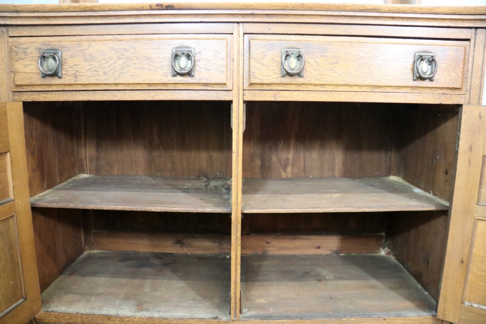 A late Victorian oak sideboard featuring a mirrored upper shelf, two drawers, and two carved panel cupboard doors. View XIII