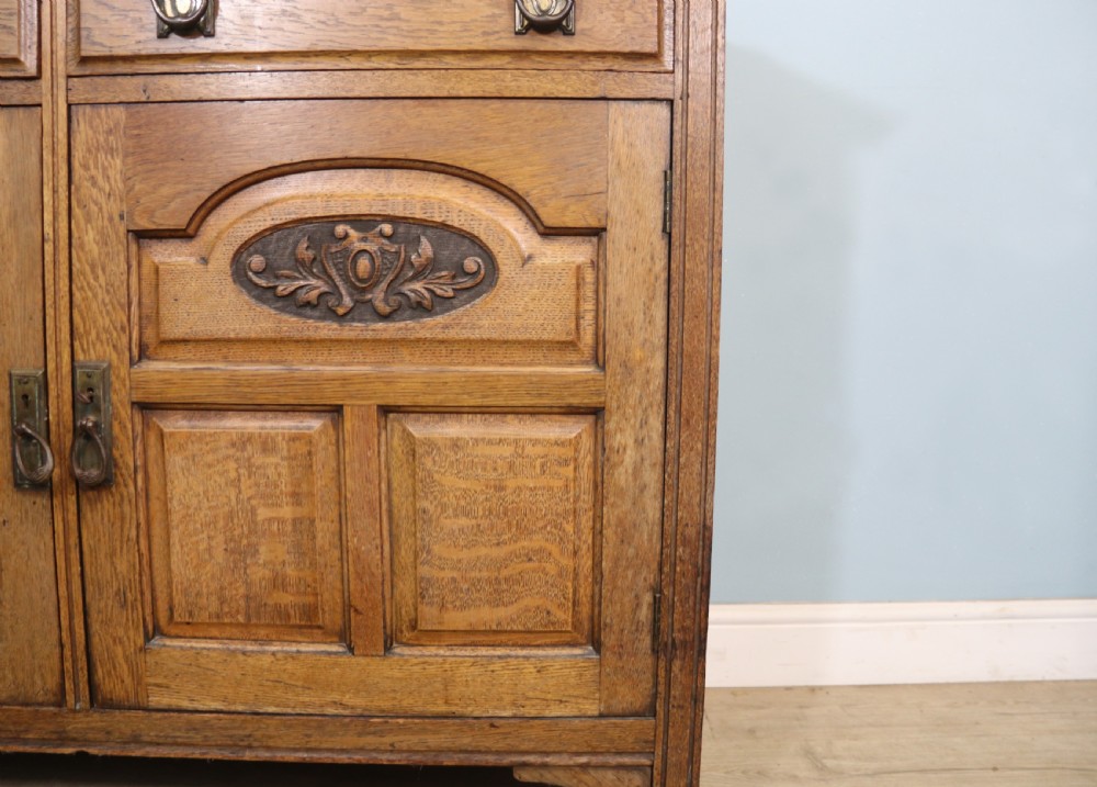 A late Victorian oak sideboard featuring a mirrored upper shelf, two drawers, and two carved panel cupboard doors. View XVI