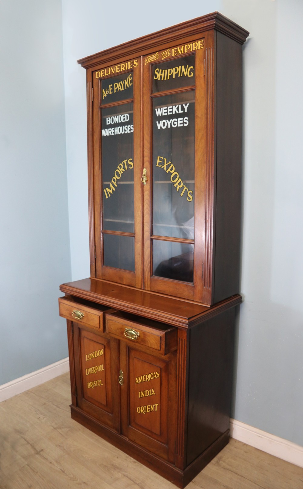 A late 19th-century warm brown walnut glazed bookcase cabinet featuring gilded sign-written trade lettering across the glass doors and lower timber panels.