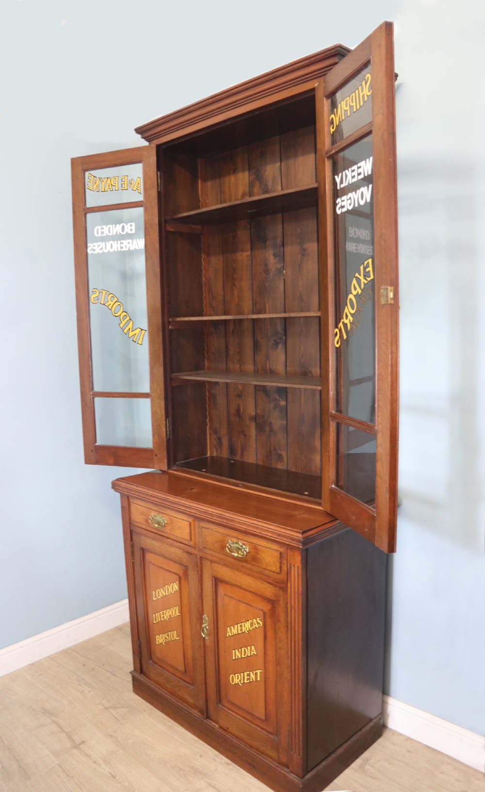 A late 19th-century warm brown walnut glazed bookcase cabinet featuring gilded sign-written trade lettering across the glass doors and lower timber panels. View II