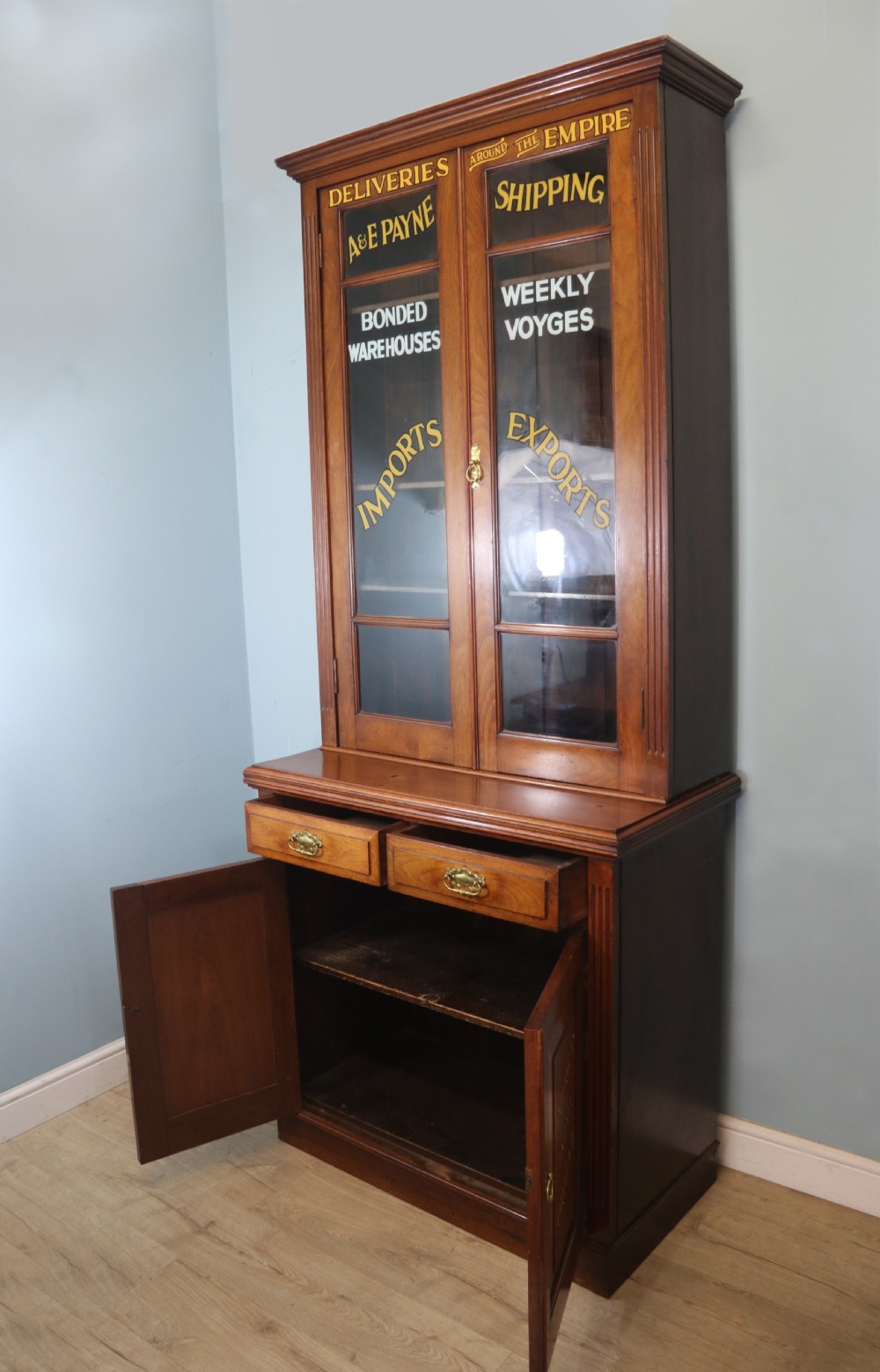 A late 19th-century warm brown walnut glazed bookcase cabinet featuring gilded sign-written trade lettering across the glass doors and lower timber panels. View III