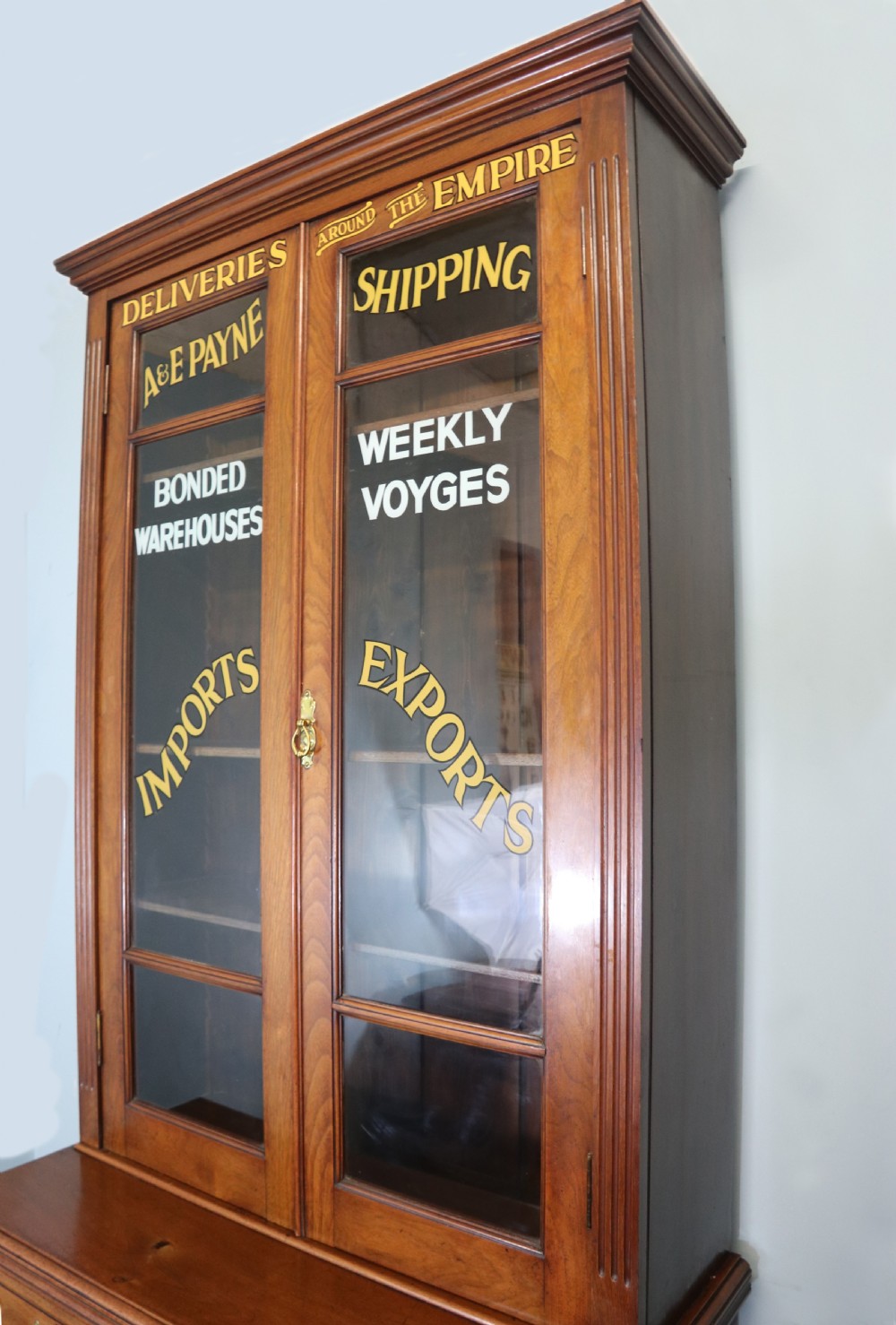 A late 19th-century warm brown walnut glazed bookcase cabinet featuring gilded sign-written trade lettering across the glass doors and lower timber panels. View IV