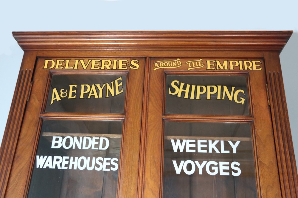 A late 19th-century warm brown walnut glazed bookcase cabinet featuring gilded sign-written trade lettering across the glass doors and lower timber panels. View V