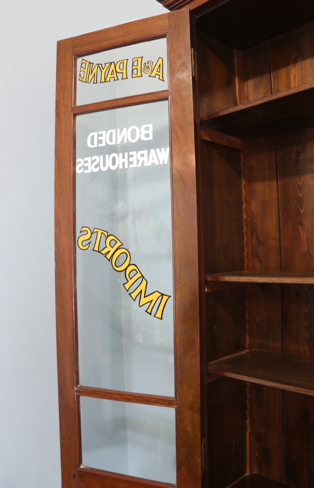 A late 19th-century warm brown walnut glazed bookcase cabinet featuring gilded sign-written trade lettering across the glass doors and lower timber panels. View VII