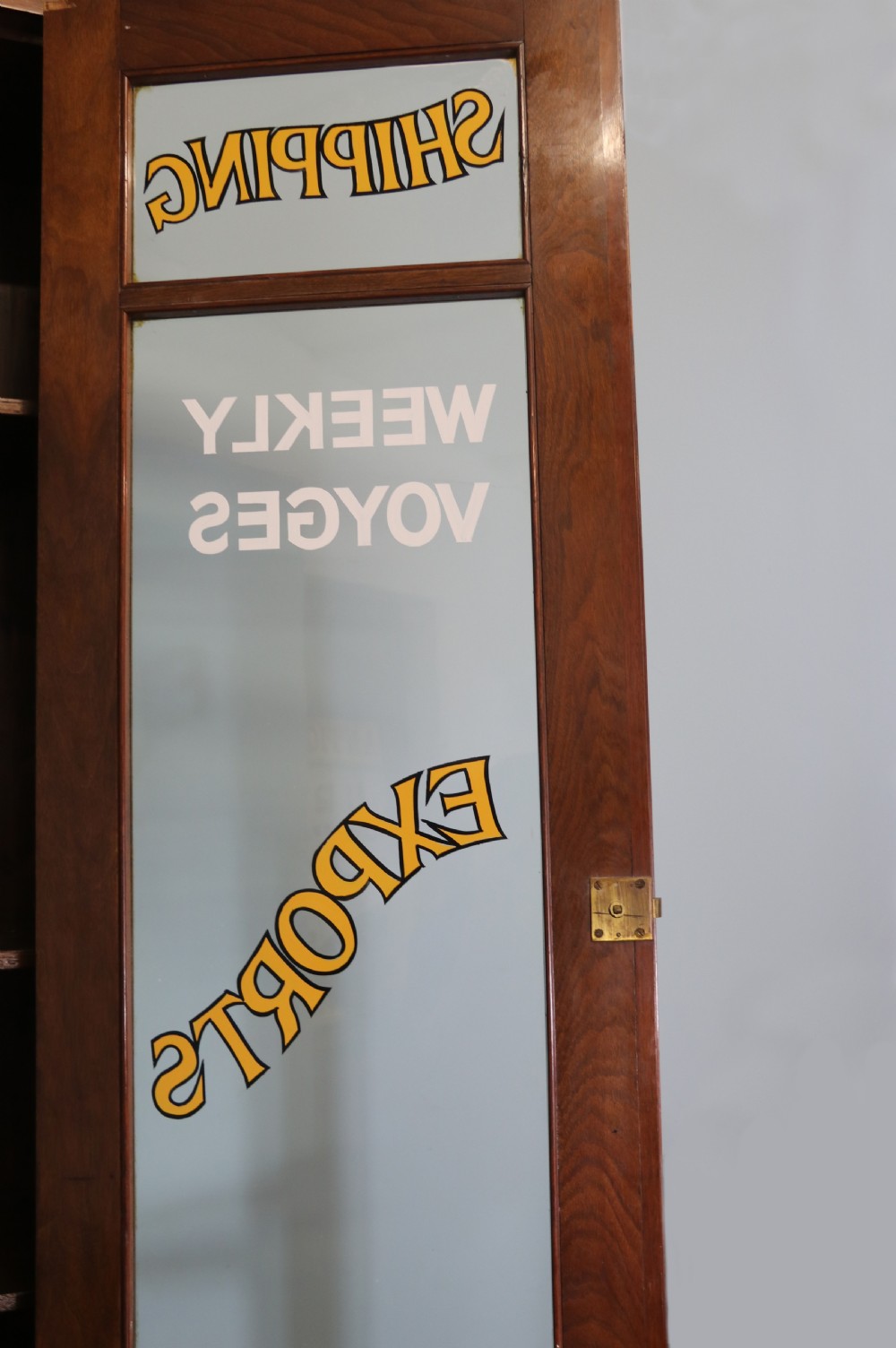 A late 19th-century warm brown walnut glazed bookcase cabinet featuring gilded sign-written trade lettering across the glass doors and lower timber panels. View VIII