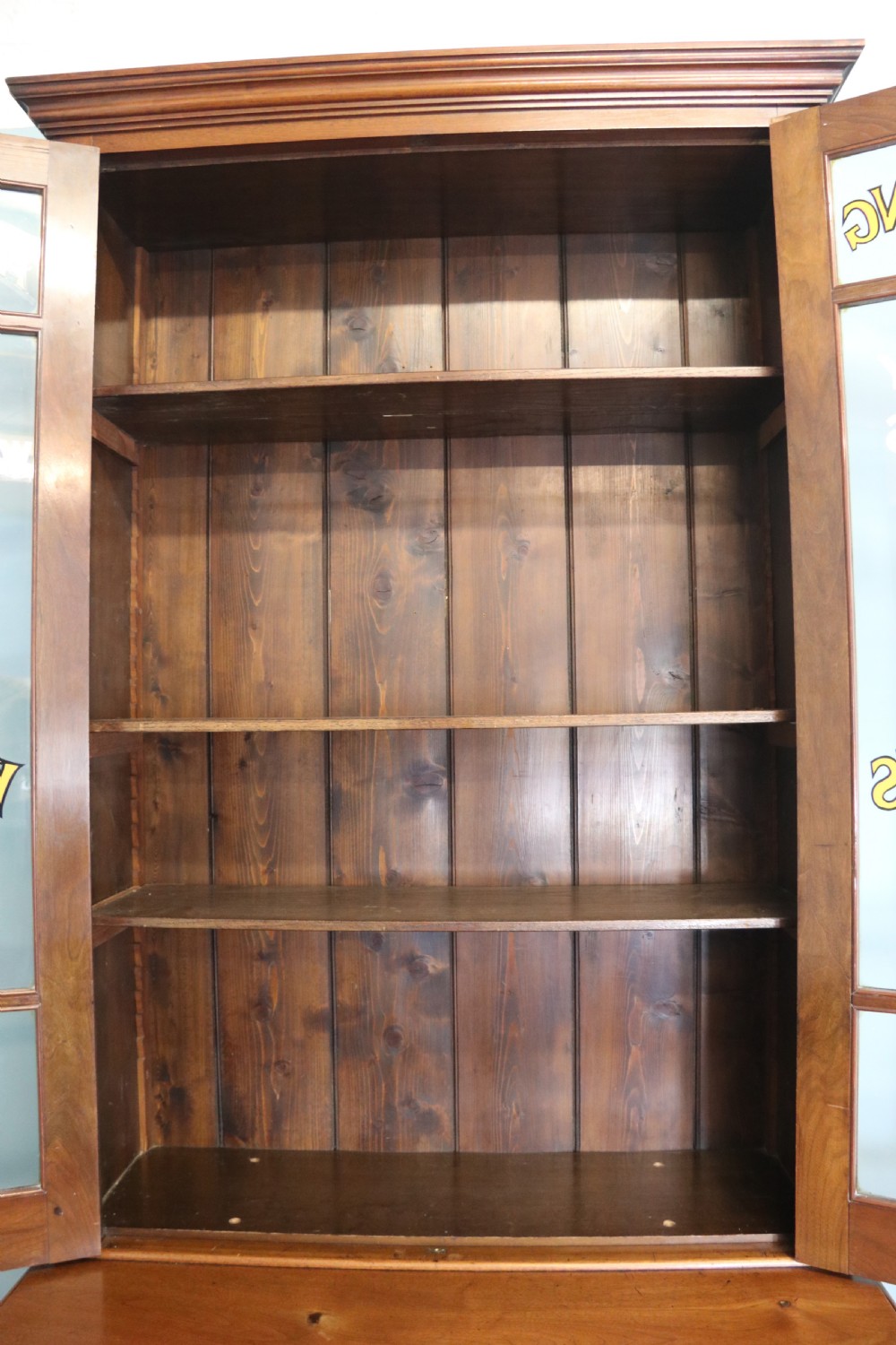 A late 19th-century warm brown walnut glazed bookcase cabinet featuring gilded sign-written trade lettering across the glass doors and lower timber panels. View IX