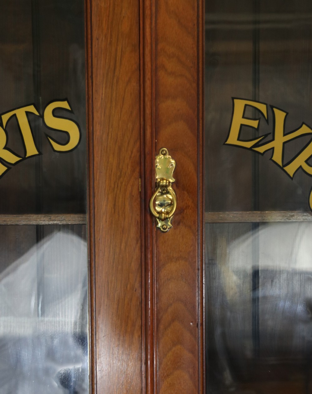 A late 19th-century warm brown walnut glazed bookcase cabinet featuring gilded sign-written trade lettering across the glass doors and lower timber panels. View XIII