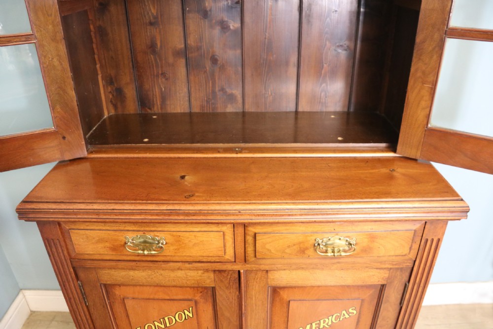 A late 19th-century warm brown walnut glazed bookcase cabinet featuring gilded sign-written trade lettering across the glass doors and lower timber panels. View XV