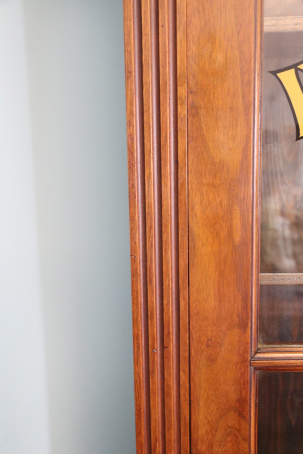 A late 19th-century warm brown walnut glazed bookcase cabinet featuring gilded sign-written trade lettering across the glass doors and lower timber panels. View XVI