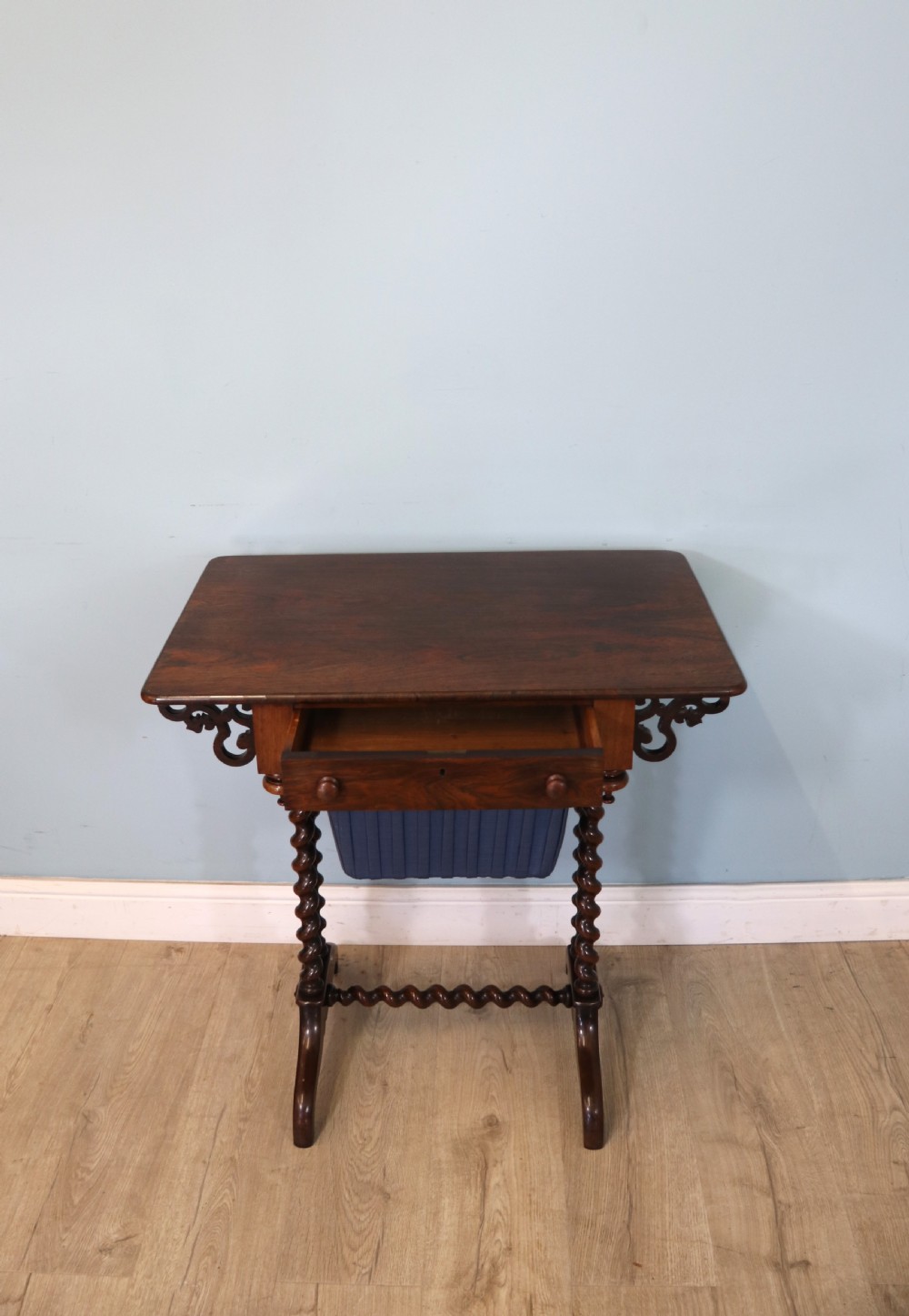 A 19th-century dark rosewood sewing table featuring barley twist legs, side fretwork brackets, a single drawer, and a blue fabric work basket below. View III