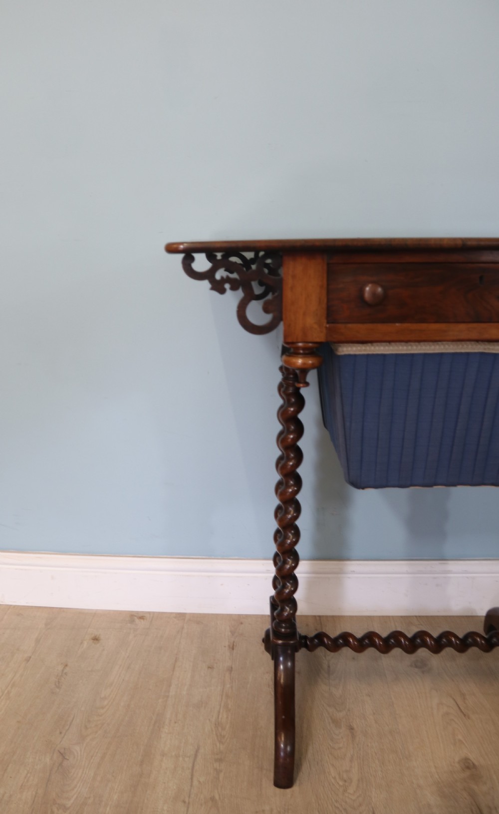 A 19th-century dark rosewood sewing table featuring barley twist legs, side fretwork brackets, a single drawer, and a blue fabric work basket below. View V