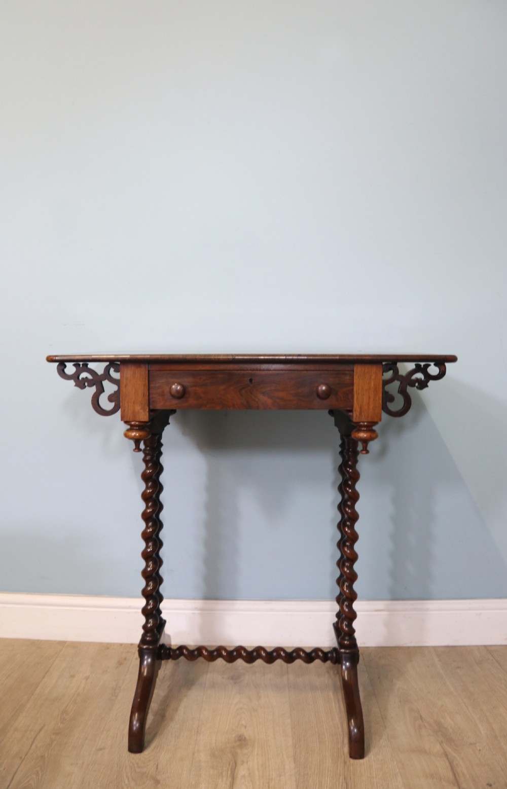 A 19th-century dark rosewood sewing table featuring barley twist legs, side fretwork brackets, a single drawer, and a blue fabric work basket below. View IX