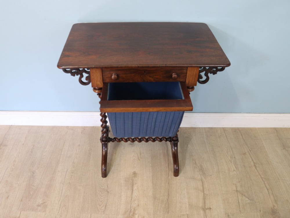 A 19th-century dark rosewood sewing table featuring barley twist legs, side fretwork brackets, a single drawer, and a blue fabric work basket below. View XI