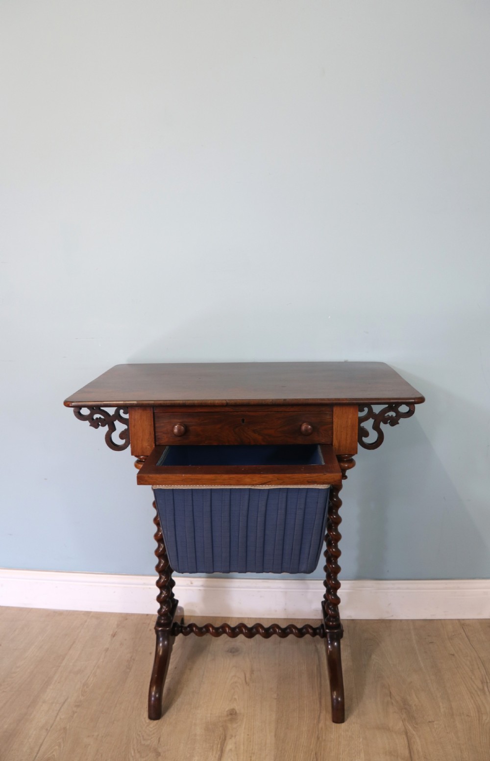 A 19th-century dark rosewood sewing table featuring barley twist legs, side fretwork brackets, a single drawer, and a blue fabric work basket below. View XII