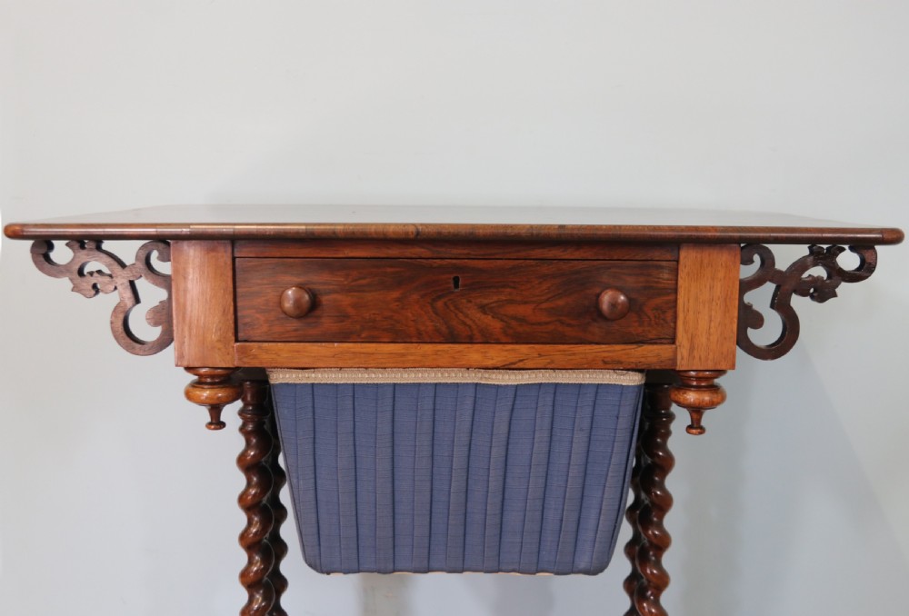 A 19th-century dark rosewood sewing table featuring barley twist legs, side fretwork brackets, a single drawer, and a blue fabric work basket below. View XIII