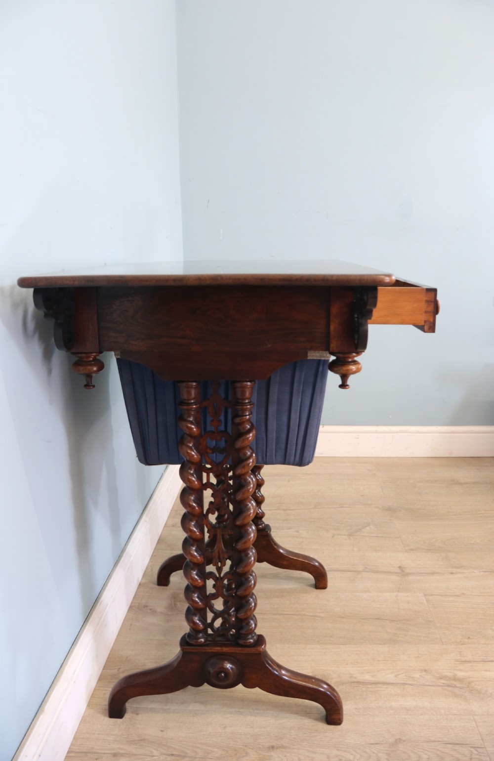 A 19th-century dark rosewood sewing table featuring barley twist legs, side fretwork brackets, a single drawer, and a blue fabric work basket below. View XIV