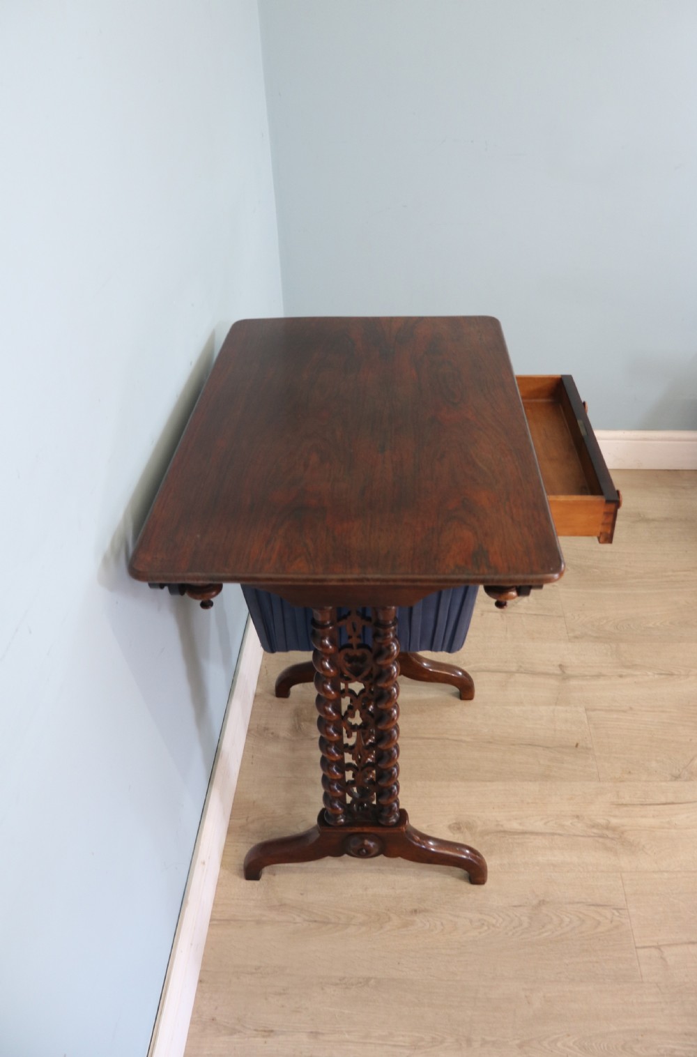 A 19th-century dark rosewood sewing table featuring barley twist legs, side fretwork brackets, a single drawer, and a blue fabric work basket below. View XV