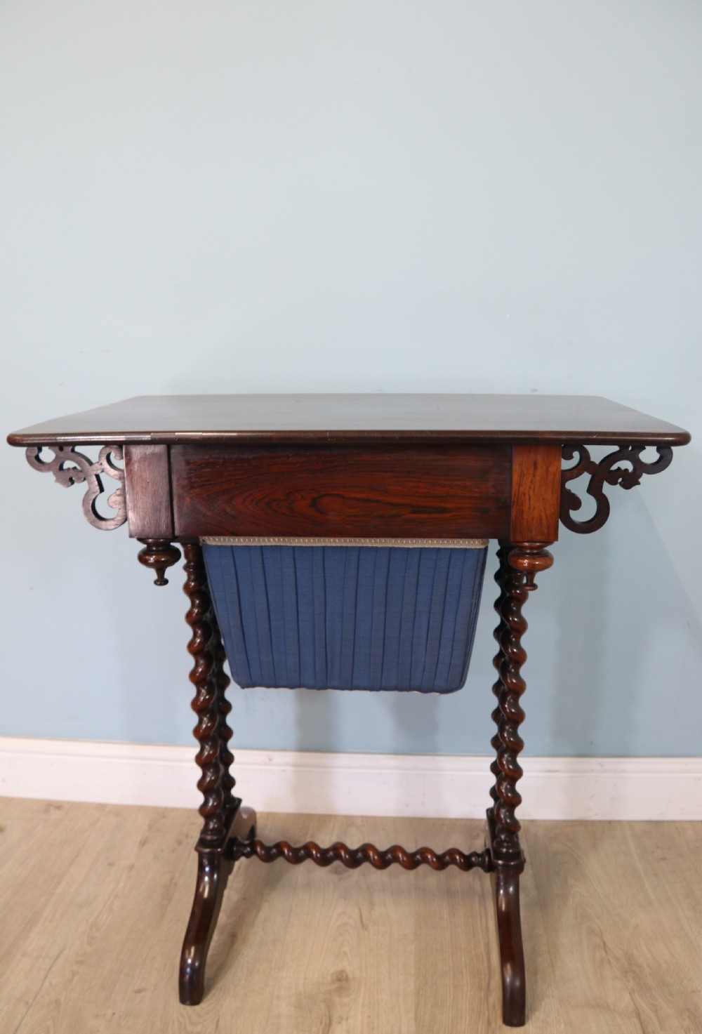 A 19th-century dark rosewood sewing table featuring barley twist legs, side fretwork brackets, a single drawer, and a blue fabric work basket below. View XVII