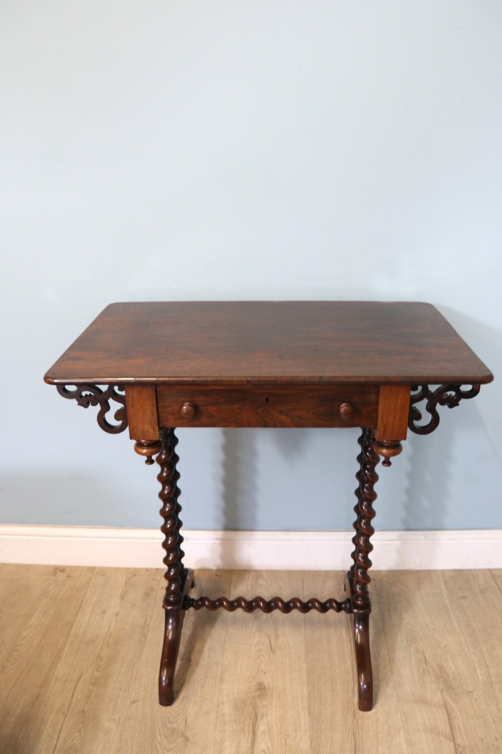 A 19th-century dark rosewood sewing table featuring barley twist legs, side fretwork brackets, a single drawer, and a blue fabric work basket below. View XXI