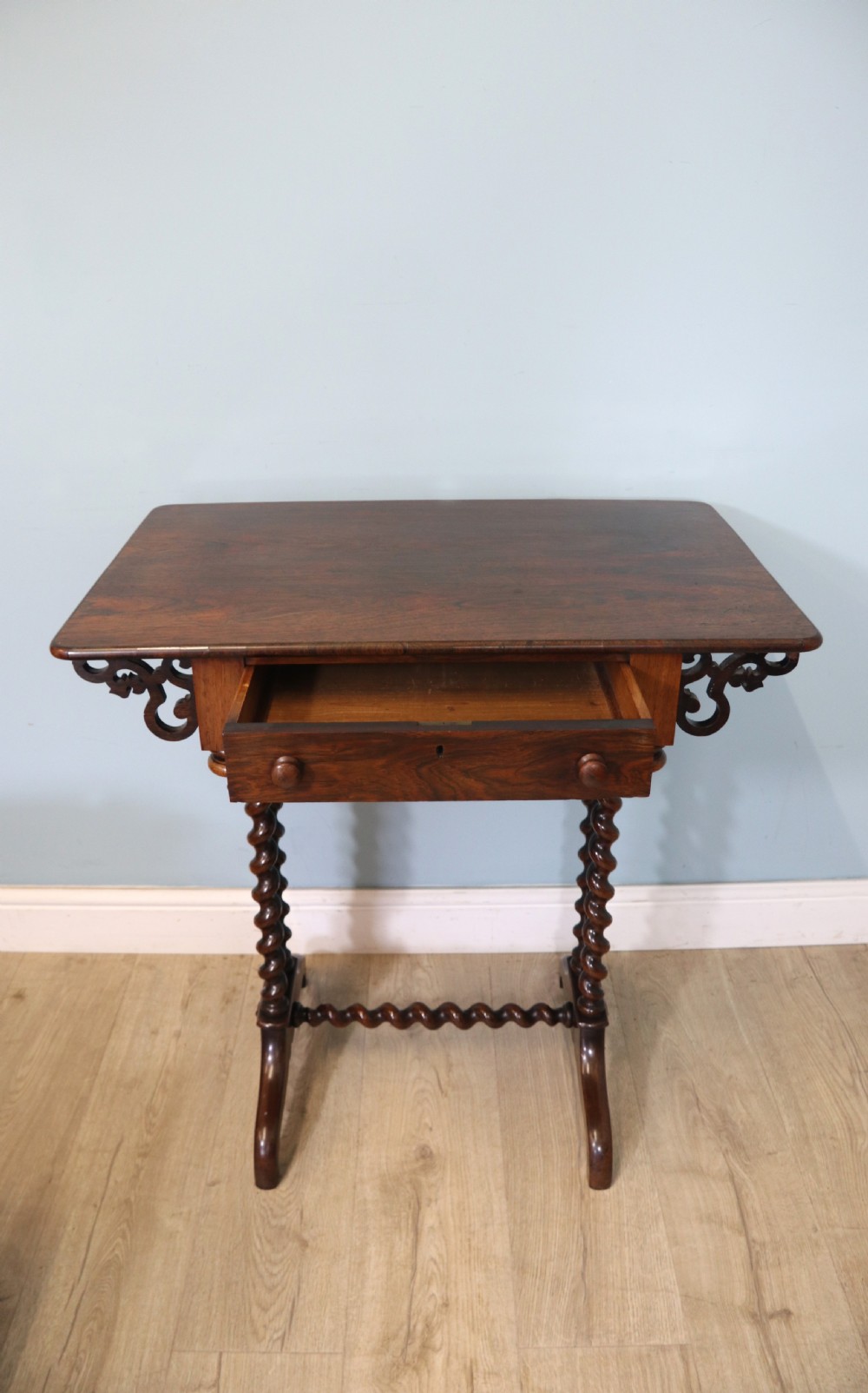 A 19th-century dark rosewood sewing table featuring barley twist legs, side fretwork brackets, a single drawer, and a blue fabric work basket below. View XXII